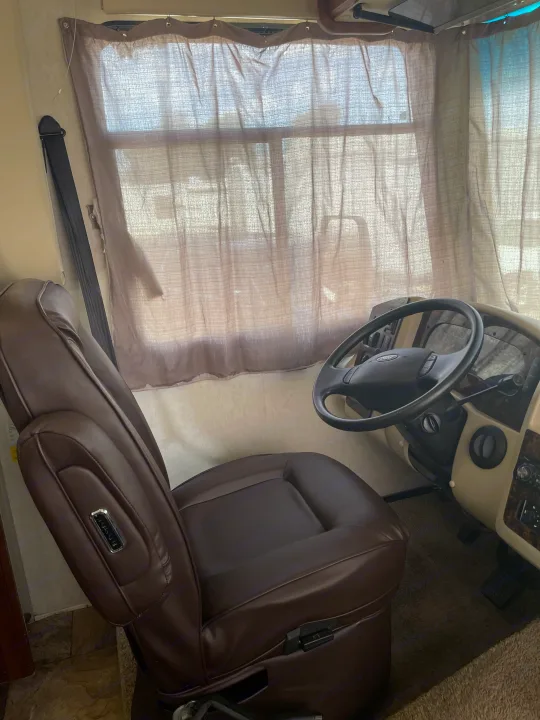 RV rental driver's area: brown leather seat, Ford steering wheel, and dashboard with sheer curtains.. Coachmen Pursuit 2014