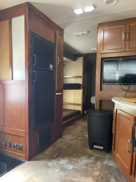 Step inside this RV rental, featuring a compact kitchen with a fridge, built-in bunk beds, and a living area with a TV.. Coachmen Pursuit 2014