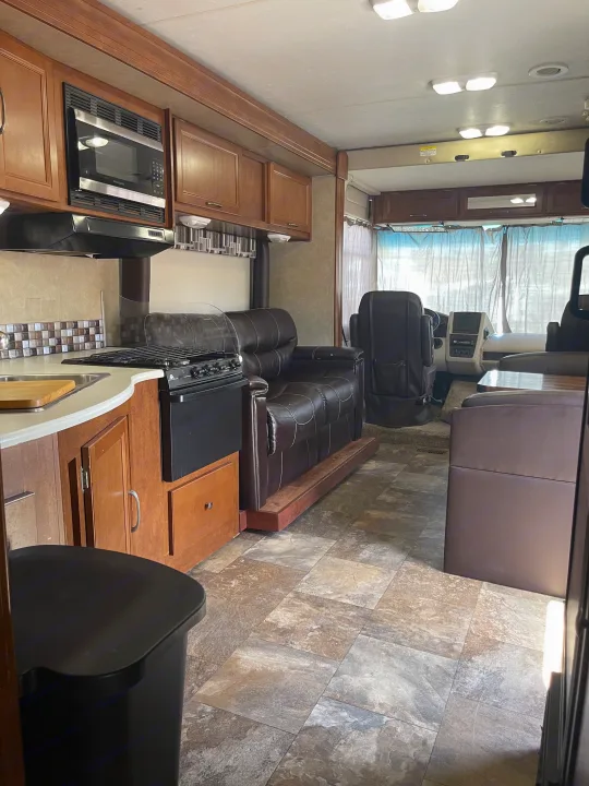 Spacious RV rental interior with a well-appointed kitchen, comfortable recliners, and driver's cabin area.. Coachmen Pursuit 2014
