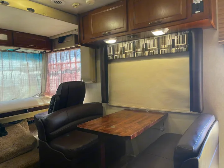 Experience comfort in this RV rental interior: a bright space with a cozy bed, a well-lit dinette, and overhead cabinets.. Coachmen Pursuit 2014