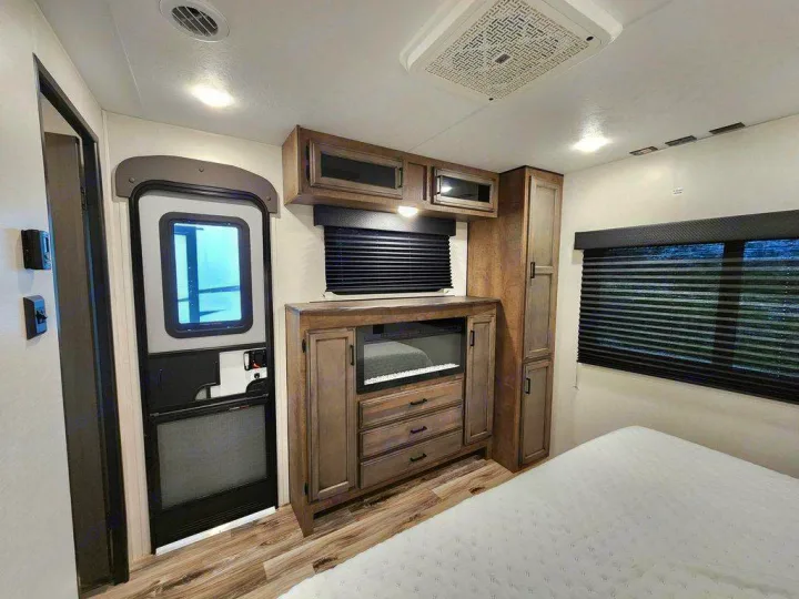 Inside an RV rental bedroom: features a cozy bed, window with blinds, storage unit with fireplace, and entry door. Perfect for travel.. SportTrek STT333VFK 2023