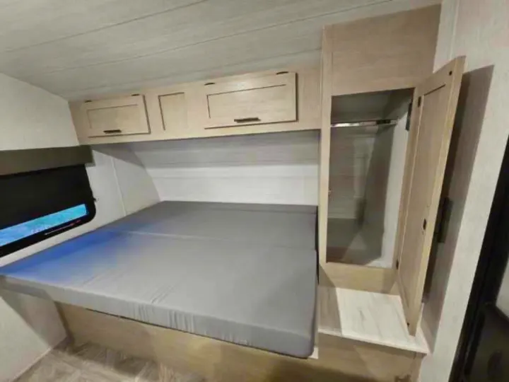 Cozy RV rental bedroom featuring a grey mattress, overhead light wood cabinets, and a tall wardrobe on the right.. Forest River Salem Cruise Lite 2024