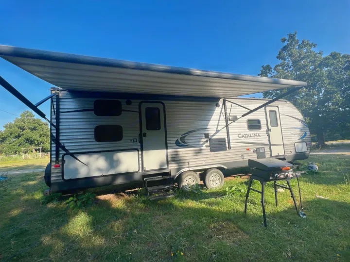 An RV rental setup: a travel trailer with an extended awning and a BlackStone griddle ready for outdoor cooking.. Coachmen 273BHS 2019