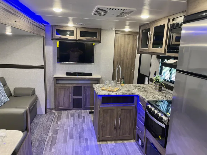 Inside a stylish rv rental: a well-appointed kitchen, cozy living room with TV & couch, all illuminated by vibrant blue LEDs.. Crossroads RV Zinger Lite 2022