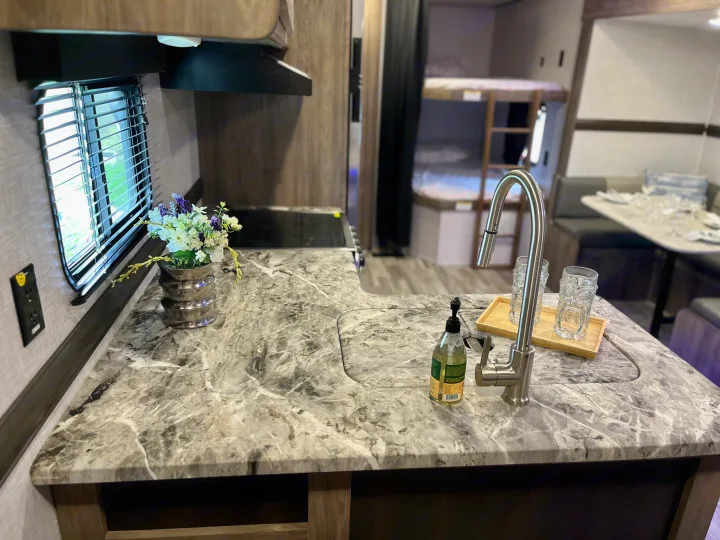 Spacious RV rental interior featuring a modern kitchen counter, sink, and dining area with bunk beds in the background.. Crossroads RV Zinger Lite 2022