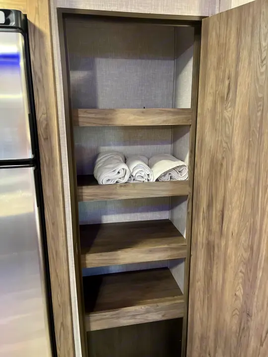 RV rental: interior view of a compact pantry cabinet with open shelves, including rolled towels, next to a refrigerator.. Crossroads RV Zinger Lite 2022