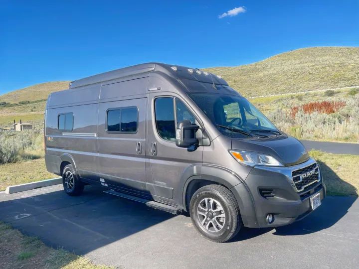 A grey Winnebago Solis RV rental camper van parked on asphalt with hills in the background under a blue sky.. Winnebago Solis 2023
