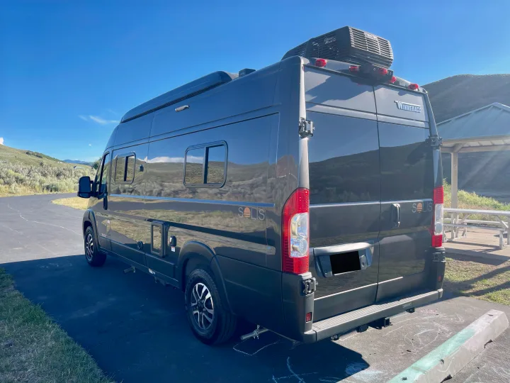Dark grey Winnebago Solis RV rental van parked on asphalt with mountains in background. Perfect for outdoor adventure.. Winnebago Solis 2023