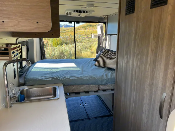 RV rental van interior with a bed, kitchen sink, and a stunning view of hills and nature from the large windows.. Winnebago Solis 2023