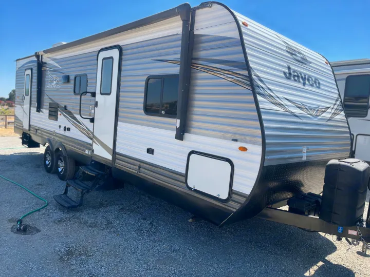 A sleek Jayco travel trailer RV rental, gray with white accents, parked on gravel under a clear sky.. Jayco Jay Flight 2018