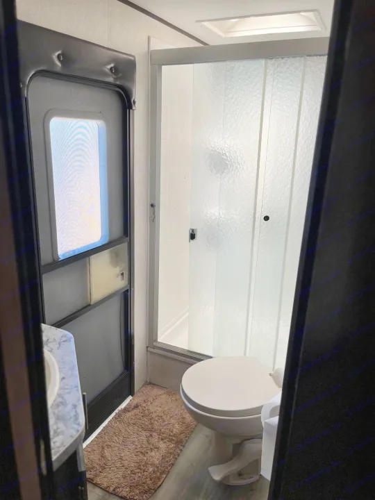 RV rental bathroom with a white toilet, frosted glass shower doors, and a sink. A brown rug covers the floor.. Jayco Jay Flight 2018