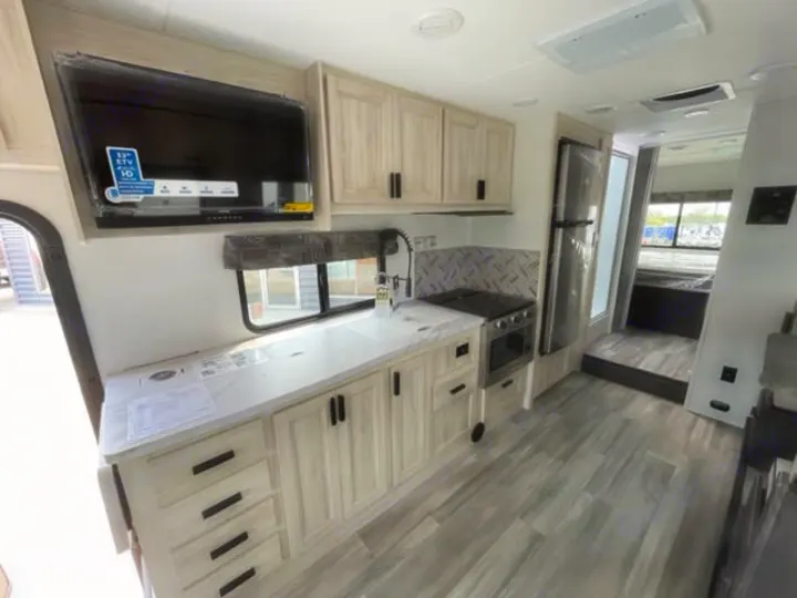 Spacious, modern RV rental interior featuring a full kitchen with light wood cabinets, appliances, and a TV, leading to the bedroom.. Forest River Sunseeker Classic 2023