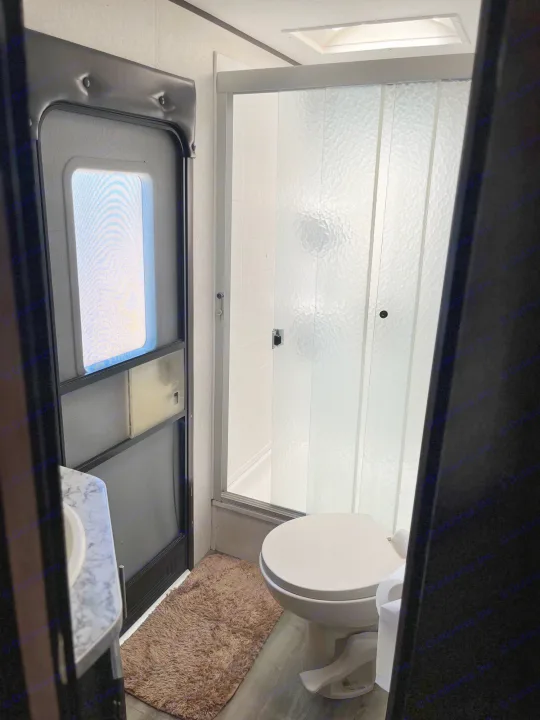 RV rental bathroom: Compact toilet, frosted glass shower, sink, and entry door with screen. A skylight provides natural light.. Jayco Jay Flight 2018