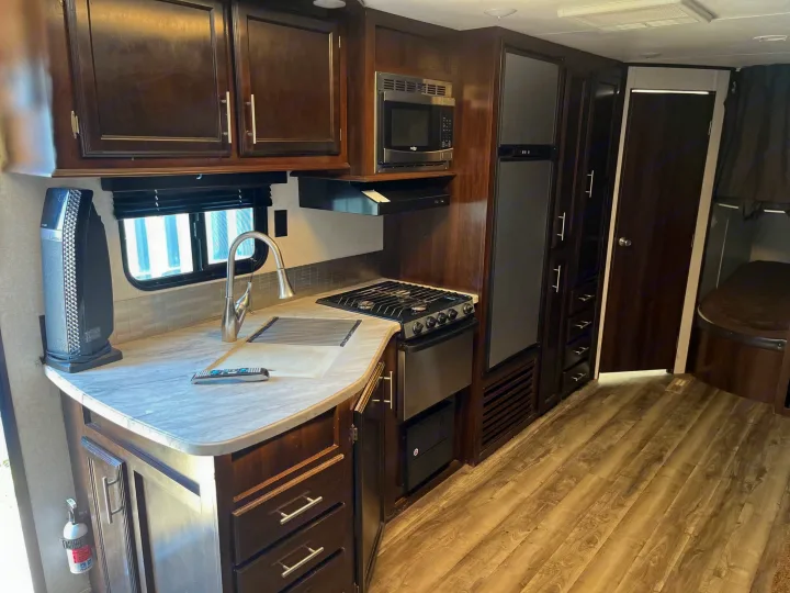 Inside an RV rental, featuring a compact kitchen with a sink, stove, microwave, and fridge, plus visible bunk beds.. Jayco Jay Flight 2018
