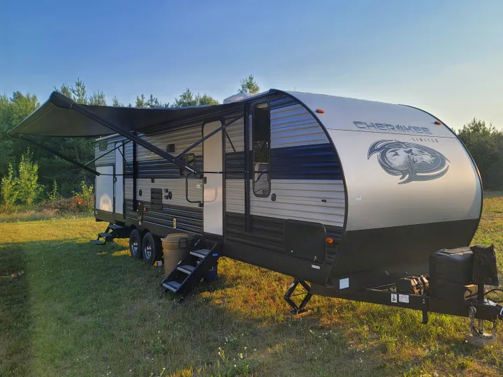 Travel trailer RV rental ready for a nature escape. Awning extended at a grassy campsite with forest backdrop.. Forest River Cherokee 2020