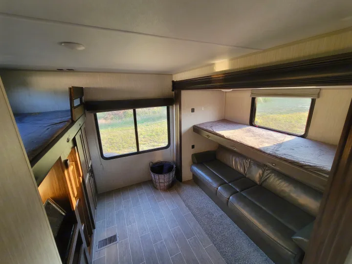 RV rental interior showing bunk beds, a dark sofa, and windows with outdoor views, offering comfortable lodging.. Forest River Cherokee 2020
