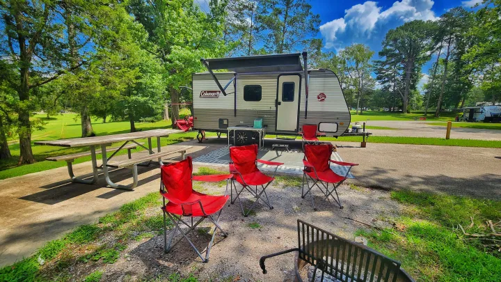 A Coleman **RV rental** ready for **camping** at a sunny park **campsite**, with red chairs, a picnic table, and a fire pit.. Coleman Lantern 2023