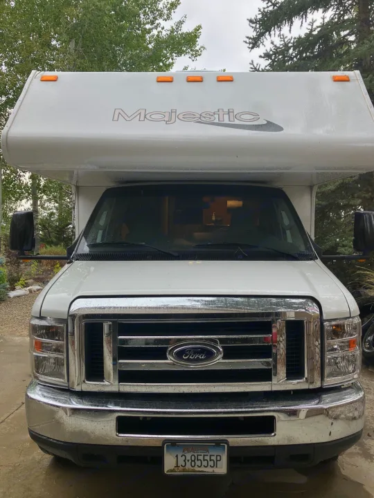 Bright white Ford Majestic Class C RV rental, parked with trees in background.. Majestic Ford 2018