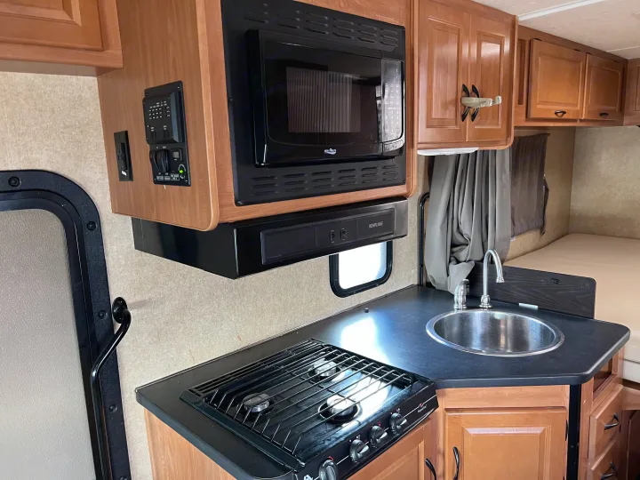 Inside an RV rental, showcasing the efficient kitchenette with microwave, stove, sink, and wall-mounted control panel.. Thor Majestic 2017