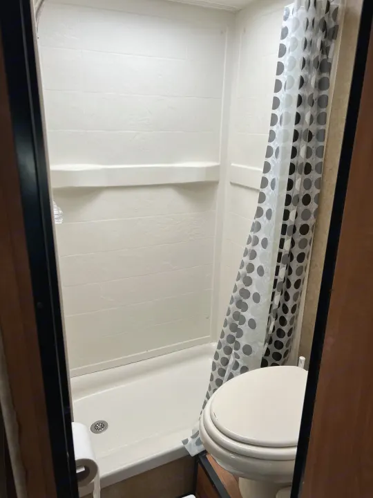Compact white shower with built-in shelf and polka dot curtain next to a toilet in an RV rental bathroom.. Thor Majestic 2017