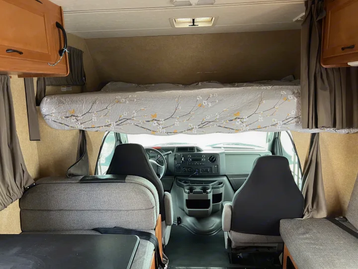 RV rental interior: View from the back showing an overhead bunk, driver's cockpit, and dinette seating with a table.. Thor Majestic 2017