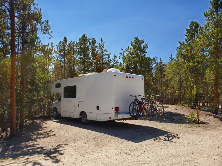 RV rental ready for adventure, parked in a sunny, tree-filled campsite with bikes on the back.. Thor Majestic 2017