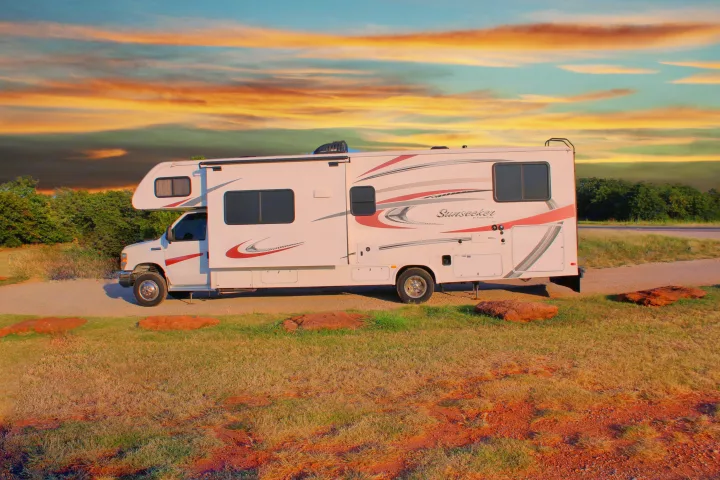 A white Sunseeker RV rental, with red and grey decals, is parked on a path against a vibrant sunset sky.. Forest River Sunseeker 2015