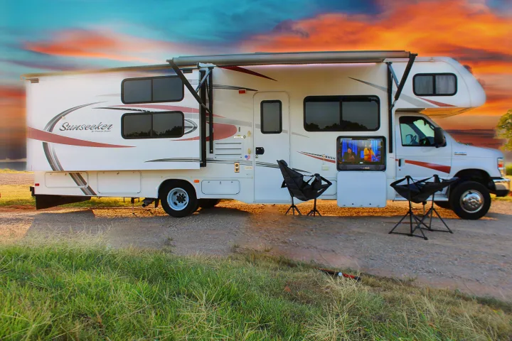 An rv rental motorhome is set up for outdoor entertainment with a TV and chairs, parked on a gravel path at sunset.. Forest River Sunseeker 2015