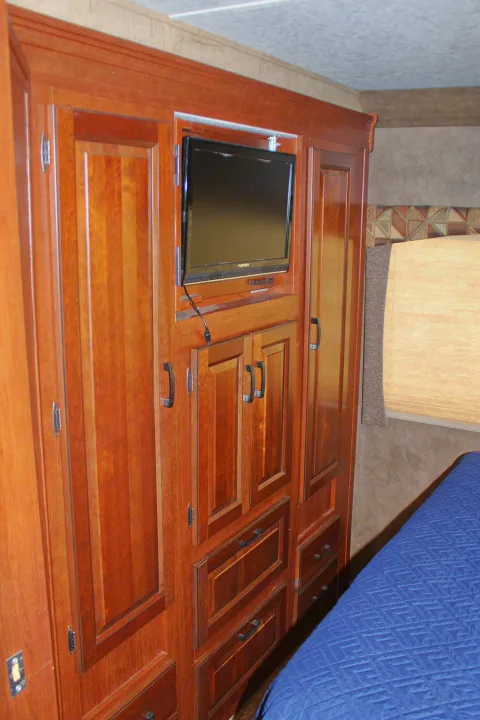 RV rental bedroom featuring sleek wood cabinetry, integrated TV, and cozy blue quilted bed for a compact, functional space.. Forest River Sunseeker 2015