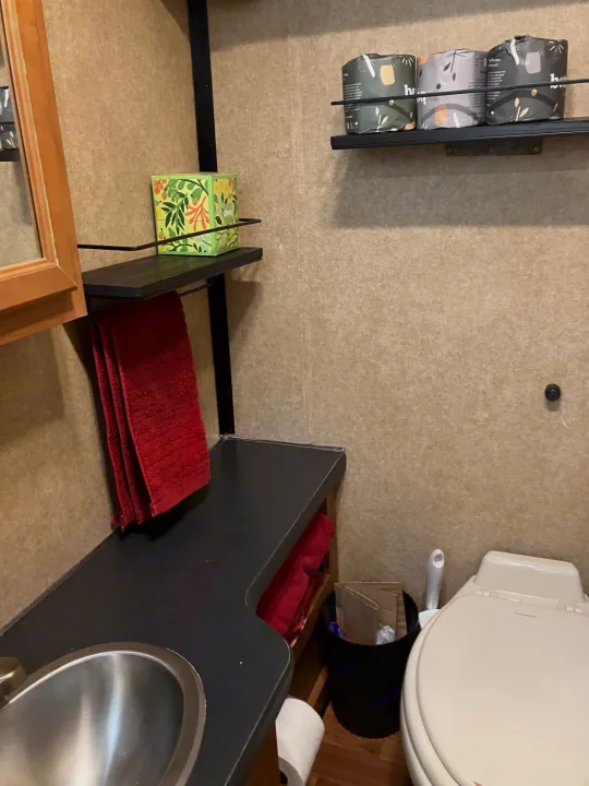 RV rental bathroom: compact space with toilet, sink, shelving holding tissue & TP, plus red towels.. Majestic Ford 2018