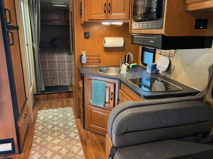 Inside an RV rental: a well-equipped kitchen, cozy bedroom with a bed, and integrated living space. Ready for your travels!. Majestic Ford 2018