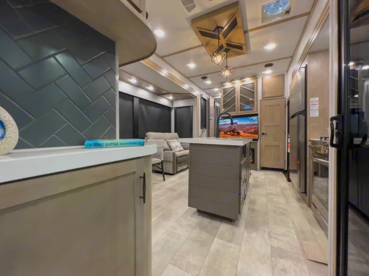 Spacious modern RV rental interior with a fully equipped kitchen, central island, cozy living area, and light wood flooring.. Grand Design Momentum 2023