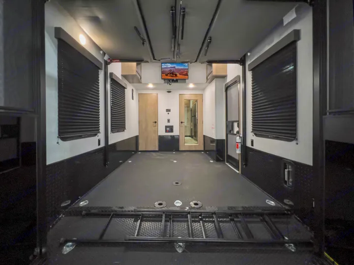 Clean RV rental toy hauler garage showing durable floor, diamond plate walls, windows, and a mounted TV.. Grand Design Momentum 2023
