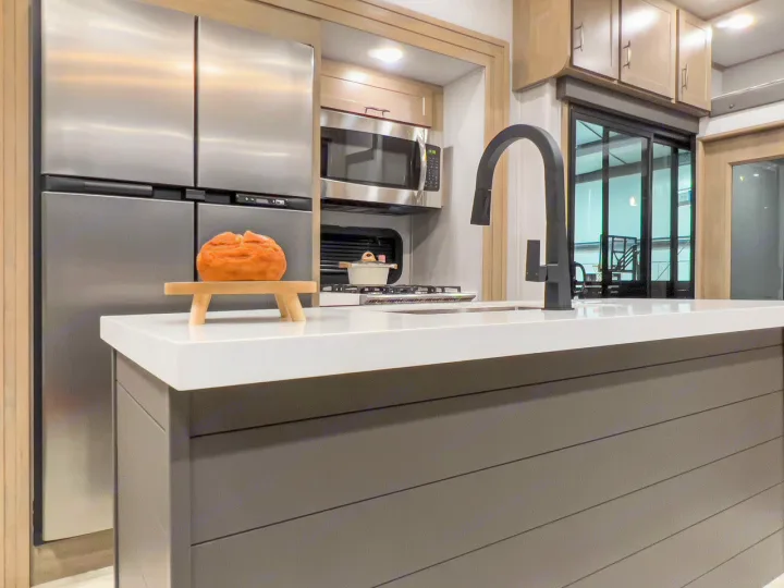 Inside a luxury RV rental: A modern kitchen with stainless appliances, an island, and sleek black faucet.. Grand Design Momentum 2023