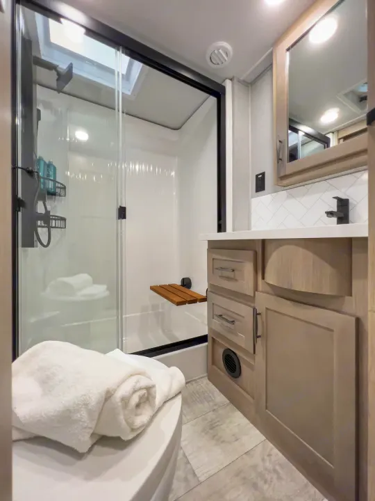 Modern RV rental bathroom: compact with a glass shower, skylight, vanity, and toilet. Bright & functional design.. Grand Design Momentum 2023