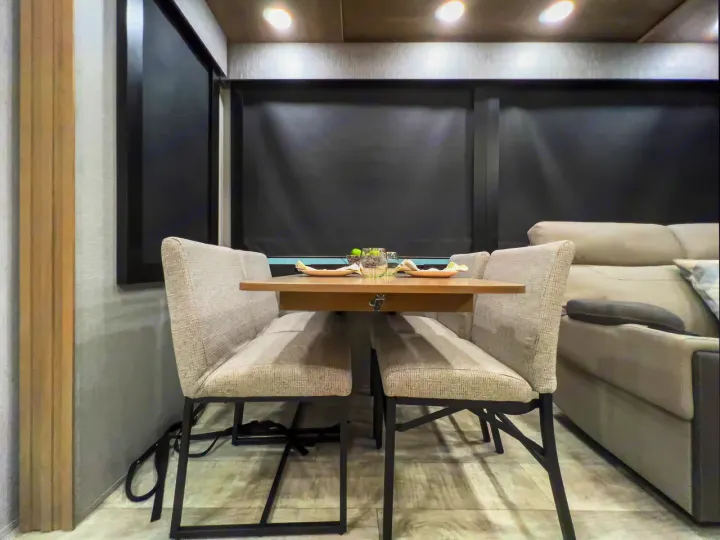 RV rental interior: modern dining area with light-colored table, two upholstered benches, and dark window shades.. Grand Design Momentum 2023