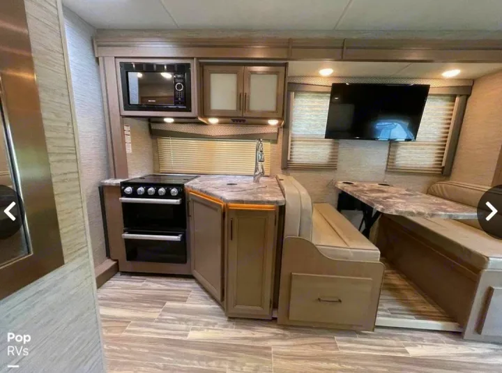 Spacious RV rental interior featuring a modern kitchen with stove, microwave, sink, and an inviting dinette with TV.. Thor Four Winds 2021