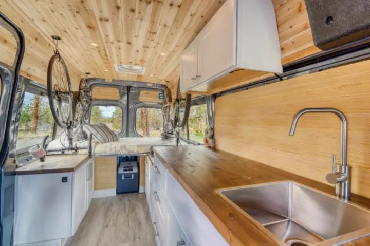 Explore this RV rental's clever interior: a wood-paneled van conversion with kitchen sink, cabinets, bed, and hanging bikes. Adventure-ready!. Mercedes-Benz Sprinter 2021