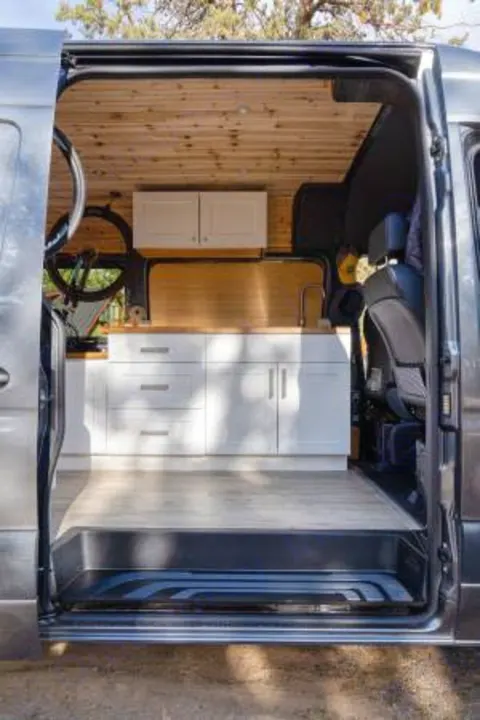 Modern RV rental interior showcasing a kitchen with white cabinets, wood countertops & ceiling, and a light-colored floor.. Mercedes-Benz Sprinter 2021
