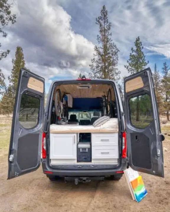 Open for adventure! This gray RV rental camper van reveals its custom interior: bed, cabinets, cooler, and bikes.. Mercedes-Benz Sprinter 2021
