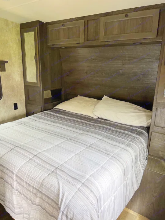 An RV rental bedroom showcasing a bed with a striped comforter, white pillows, and dark wood cabinetry.. Eclipse Recreational Vehicles Iconic 2018