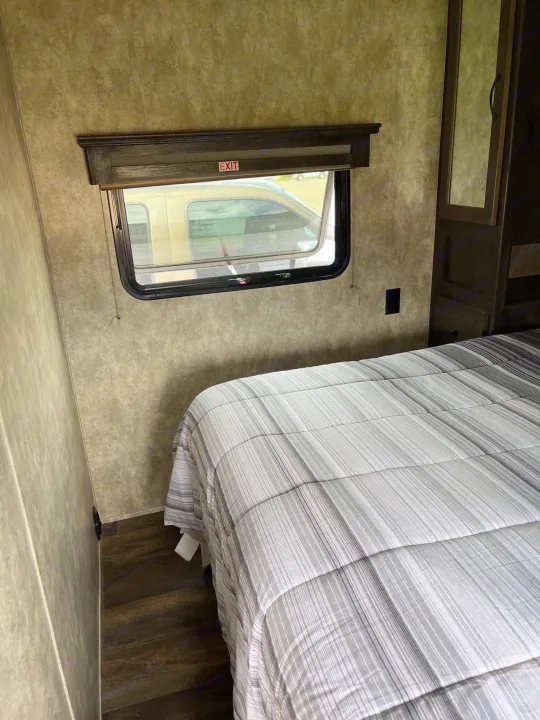 RV rental bedroom with striped bed, exit window, and wood-look floor. Ready for your next travel adventure!. Eclipse Recreational Vehicles Iconic 2018