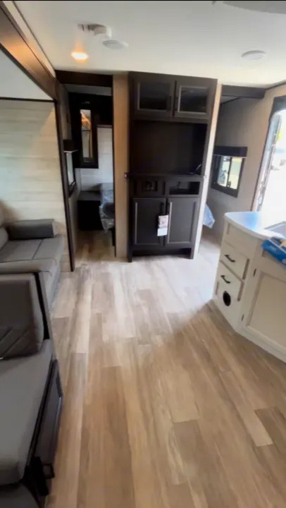 Modern RV rental interior: light wood-look floor, gray sofa, dark cabinetry, and a white kitchen counter.. Jayco Jay Flight 2023