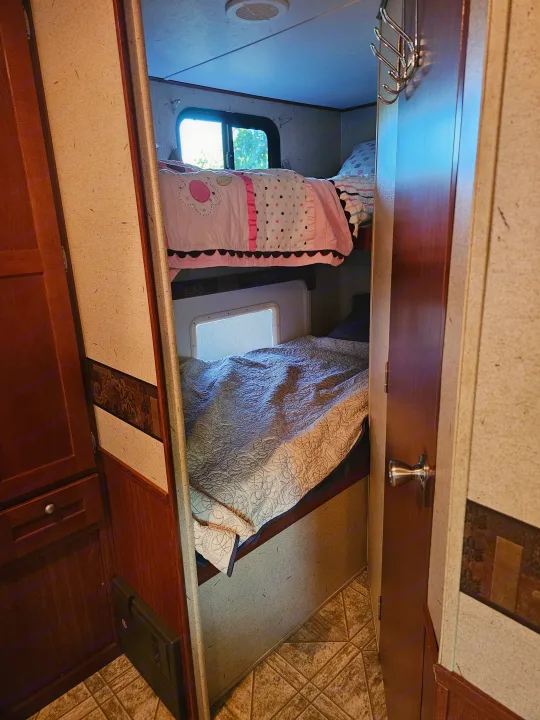 RV rental interior with cozy bunk beds: a top bed featuring pink bedding, and a bottom bed with gray quilting.. Crossroads RV Zinger 2010