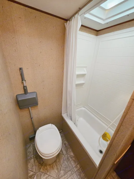 Compact rv rental bathroom with white toilet, shower/tub, curtain, and skylight. Features textured brown walls and patterned floor.. Crossroads RV Zinger 2010