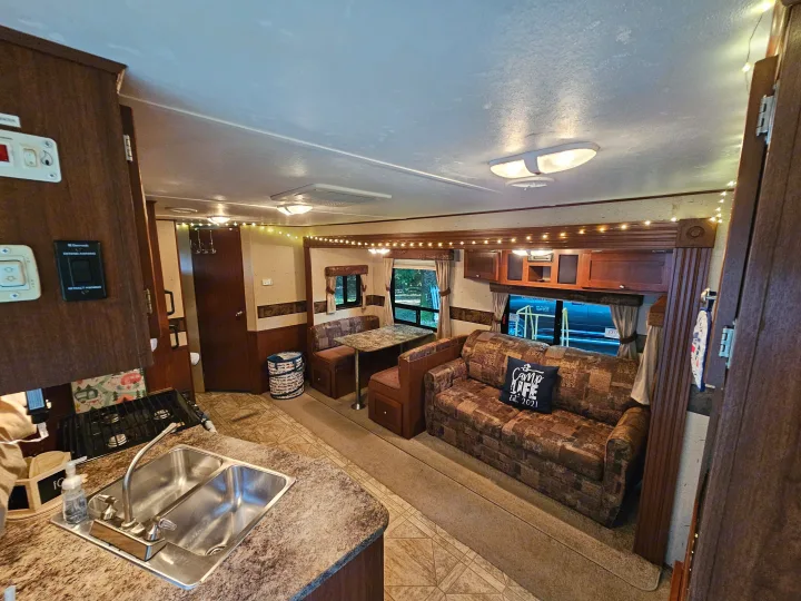 Inside a cozy RV rental: kitchen counter, dinette, and sofa visible, complete with warm string lights.. Crossroads RV Zinger 2010