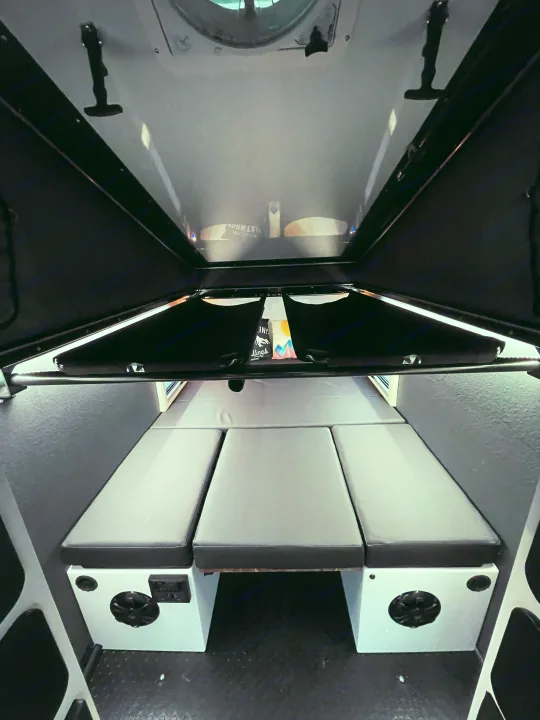 Explore the compact RV rental interior, featuring a versatile sleeping area with three gray cushions and built-in amenities.. Mission Overland Summit 2022