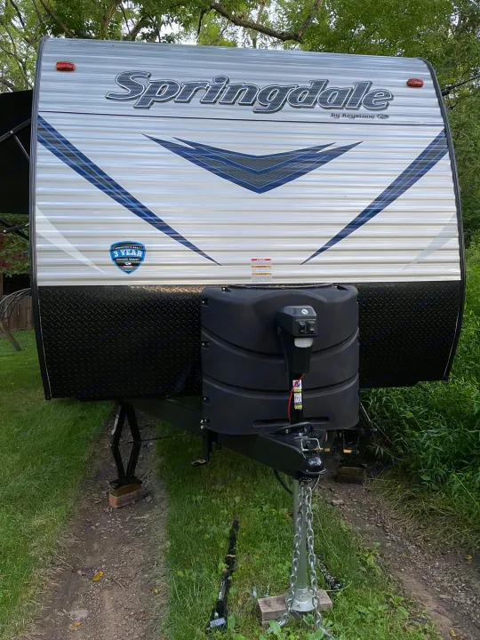 Front of a white Springdale RV rental, showing blue graphics, black diamond plate, propane tank, and hitch.. Keystone RV Springdale 2018