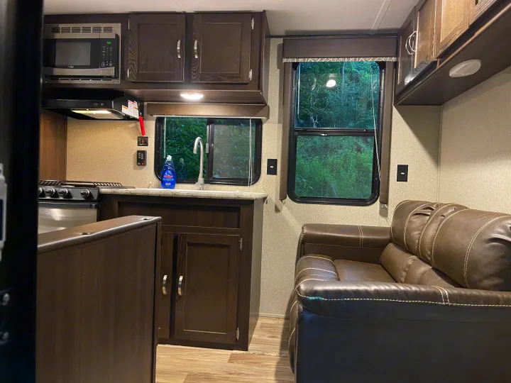Interior of an RV rental: a well-equipped kitchen with microwave and sink, alongside a comfortable brown sofa.. Keystone RV Springdale 2018