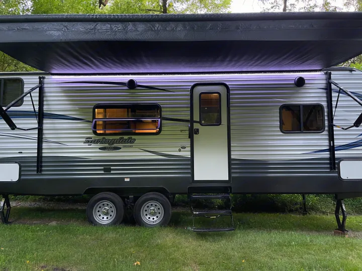 This RV rental travel trailer is set up at a campsite with its awning extended and lights on.. Keystone RV Springdale 2018